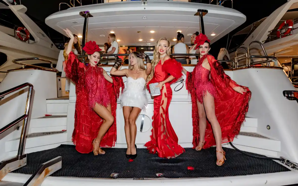 Four stylish women confidently pose aboard a yacht, ready to set off on a glamorous yacht party cruise.