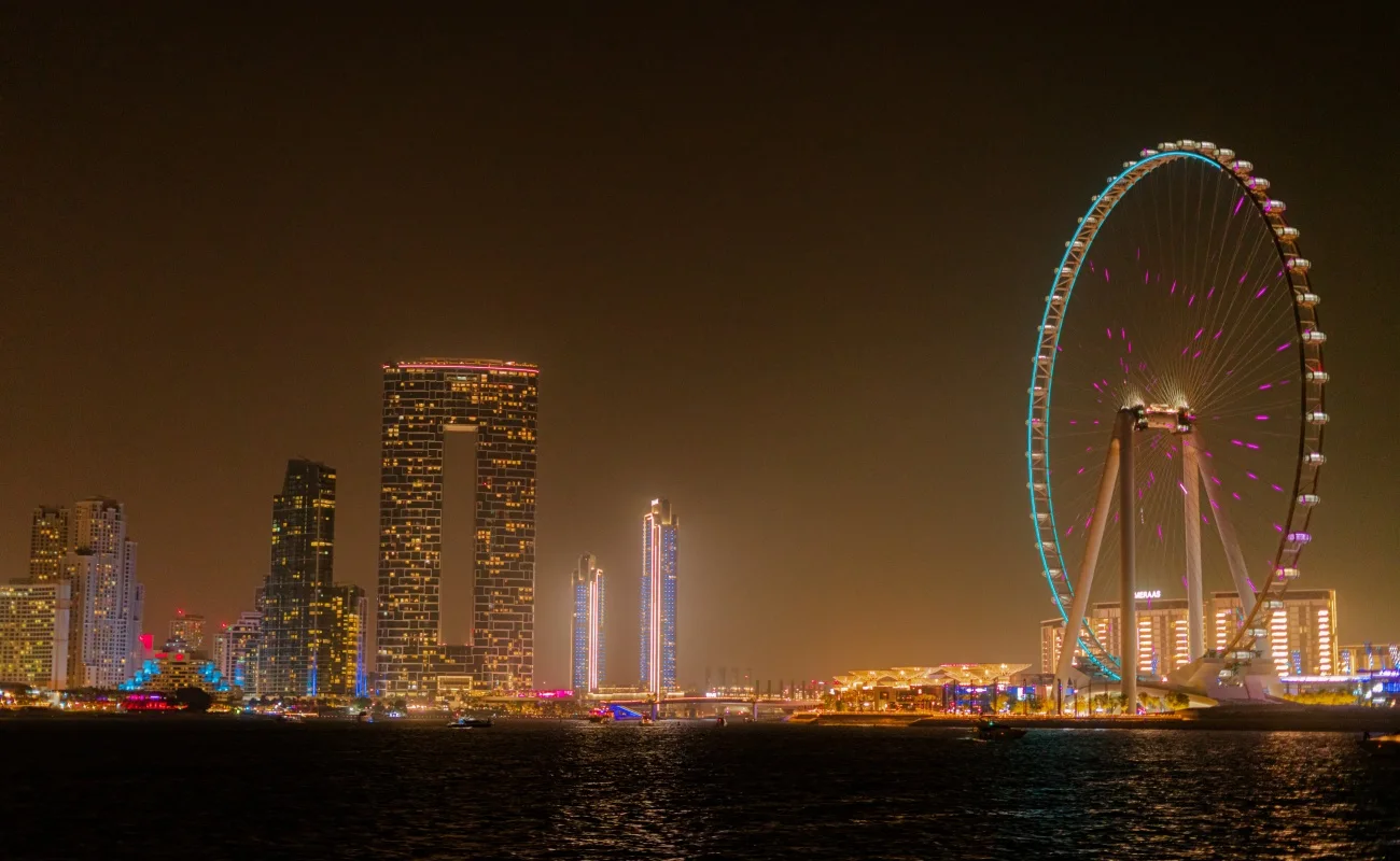 Ain Dubai illuminated at night with Dubai skyline in the background.